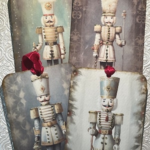 May include: Four vintage-style Christmas gift tags featuring illustrations of nutcracker soldiers. Each tag is decorated with a red ribbon and features a different nutcracker soldier in a white or blue uniform with gold accents.