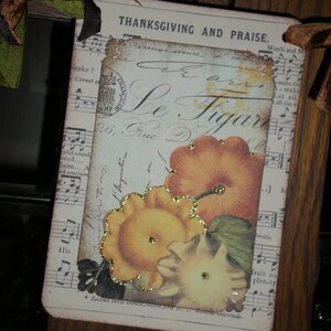 Pode incluir: Uma etiqueta retangular com tema de A&ccedil;&atilde;o de Gra&ccedil;as com as palavras "THANKSGIVING AND PRAISE". Apresenta um design vintage com elementos florais e de notas musicais, e imagens de ab&oacute;boras. A etiqueta &eacute; adornada com glitter dourado e fita.