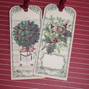 May include: Two vintage-style Christmas gift tags with red ribbon. One tag features a holly sprig with red berries and the text "A Very Happy Christmas To From". The other tag features a sprig of mistletoe with a bell and a blank space for writing.