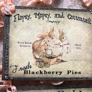 May include: A vintage-style sign with a brown background and black border. It features a drawing of three bunnies baking and the text "Hopsy, Mopsy, and Cottontail Company" and "Fresh Blackberry Pies".