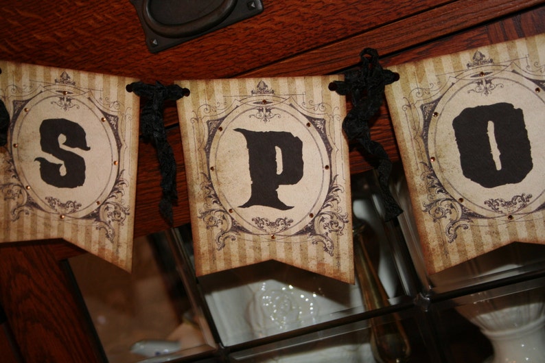 May include: A decorative banner featuring three rectangular pennants with a vintage-style beige and brown striped background. Each pennant displays a large black letter, spelling out SPO, framed by ornate dark brown filigree and small gold studs.