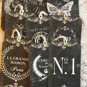 May include: A set of black and white gift tags with various Parisian themed designs. The tags feature text such as "Hotel Royal", "La Grande Maison", "Carte Postale", and "Chateau de Versailles".