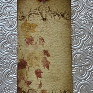 May include: A vintage-style gift tag with a brown background and a design of autumn leaves in shades of red, orange, and yellow. The tag has a decorative border and a hole at the top for hanging.