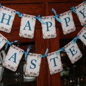 May include: A blue and white banner with the words "Happy Easter" on it. The banner is made of paper and has a floral design.
