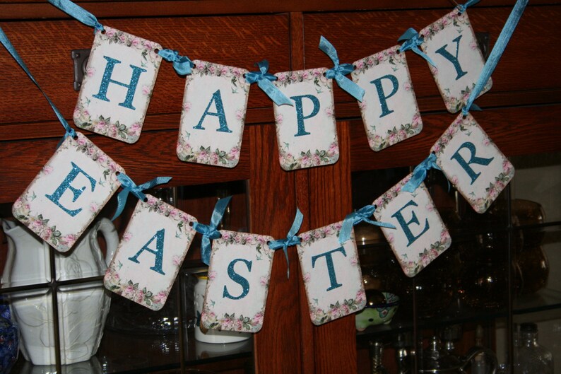 May include: A blue and white banner with the words "Happy Easter" on it. The banner is made of paper and has a floral design.