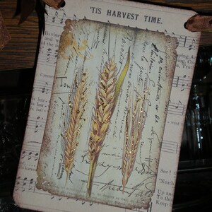 Pode incluir: Um cart&atilde;o retangular com um design vintage com espigas de trigo e escrita. O cart&atilde;o tem uma borda ondulada e o texto "'TIS HARVEST TIME". O fundo inclui notas musicais e texturas de papel envelhecido.