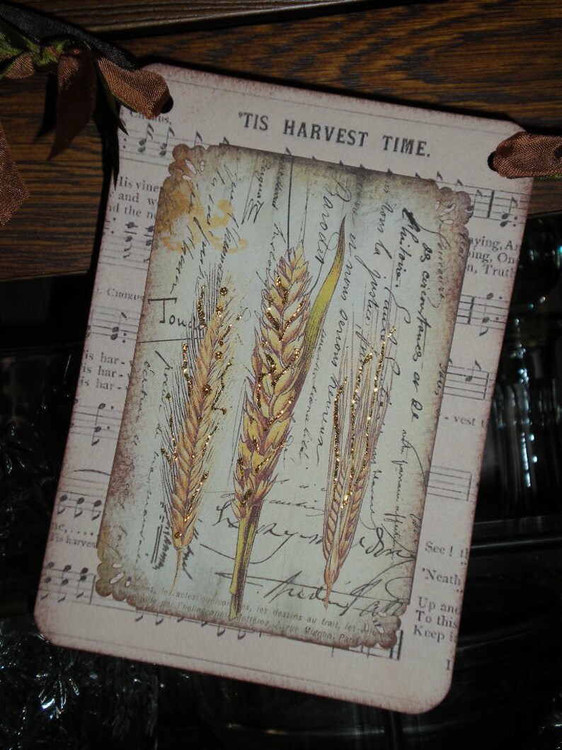 Pode incluir: Um cart&atilde;o retangular com um design vintage com espigas de trigo e escrita. O cart&atilde;o tem uma borda ondulada e o texto "'TIS HARVEST TIME". O fundo inclui notas musicais e texturas de papel envelhecido.