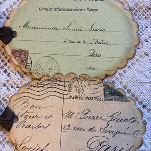 Puede incluir: Dos postales de estilo vintage con bordes festoneados y lazos de cinta marr&oacute;n. Las postales presentan texto manuscrito en franc&eacute;s, sellos y matasellos. La tarjeta superior est&aacute; dirigida a Mademoiselle Louise Guinon, y la inferior a M. Pierre Guiotat, ambos en Par&iacute;s.