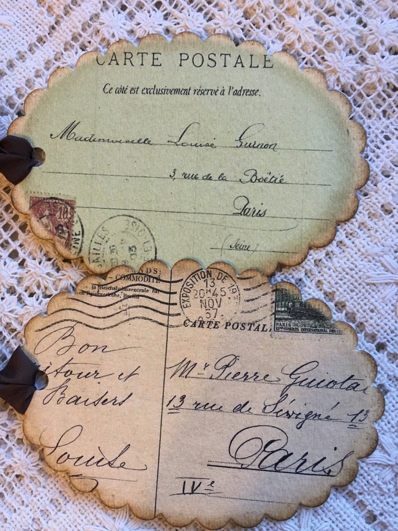 Puede incluir: Dos postales de estilo vintage con bordes festoneados y lazos de cinta marr&oacute;n. Las postales presentan texto manuscrito en franc&eacute;s, sellos y matasellos. La tarjeta superior est&aacute; dirigida a Mademoiselle Louise Guinon, y la inferior a M. Pierre Guiotat, ambos en Par&iacute;s.