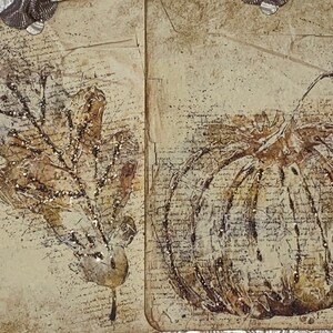Op de afbeelding: Twee decoratieve labels met herfstthema's. E&eacute;n toont een gedetailleerd blad, de andere een pompoen. Beide zijn in bruin- en beigetinten, met een vintage, getextureerde uitstraling. Glitteraccenten voegen sprankeling toe. De labels zijn versierd met zilveren lint.