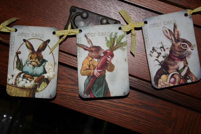 May include: A banner with three vintage postcards featuring illustrations of rabbits. The postcards are decorated with yellow and white gingham ribbon and the text "Post Card".