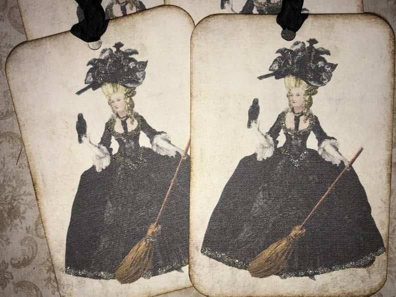 May include: Vintage-style gift tags featuring a woman in a black gown, holding a crow and a broom. The woman has blonde hair and wears a large black hat. The tags have a distressed, aged appearance with a black ribbon.