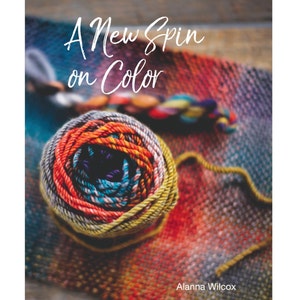 Può includere: Primo piano di un gomitolo di filato colorato su uno sfondo di tessuto tessuto. Il filato è un mix di arancione, giallo, blu e viola. Il testo "A New Spin on Color" è scritto in bianco sopra il gomitolo di filato. Il testo "Alanna Wilcox" è scritto in bianco nella parte inferiore dell'immagine.