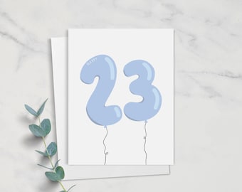 May include: Happy 23rd birthday card with blue balloon numbers. The card is white with black text.