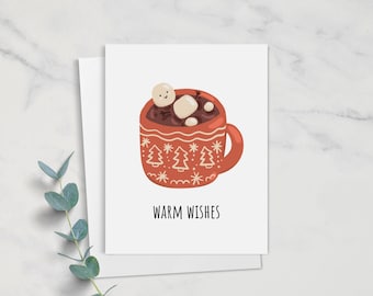 May include: Greeting card with a red mug of hot chocolate, marshmallows, and the text "Warm Wishes." The mug has a festive design with trees and snowflakes. The card is on a white background with eucalyptus.