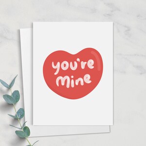 May include: A white card with a red heart shape that says "you're mine" in pink lettering.