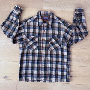 May include: A long-sleeved plaid shirt in shades of blue, brown, and white. The shirt features two chest pockets, a button-down front, and a collar. The fabric appears to be a soft, woven material.