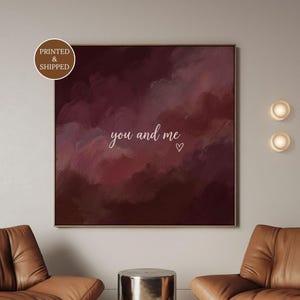 May include: A square wall art piece featuring a deep burgundy and dark red abstract painted background with the white cursive text you and me and a small heart outline. A circular badge in the top left corner contains the text PRINTED & SHIPPED.