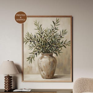 May include: A framed wall art print featuring a beige ceramic vase filled with green olive branches and dark olives. The artwork has a neutral, painterly aesthetic with soft brushstrokes and a light background, presented in a wooden frame.
