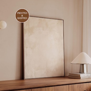 Puede incluir: Una pieza de arte mural rectangular con un diseño abstracto texturizado en tonos neutros beige y crema, encerrada en un marco fino de color marrón oscuro. La obra muestra un patrón de superficie sutil y moteado con suaves variaciones de color.