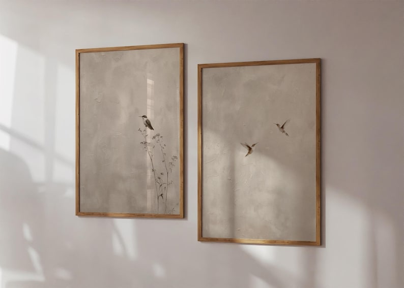 Op de afbeelding: Twee ingelijste kunstdrukken met een neutraal kleurenpalet. E&eacute;n print toont een vogel op een plant, de andere toont drie vogels in vlucht. De lijsten hebben een warme houttint, die de zachte, gedempte achtergrond aanvult.