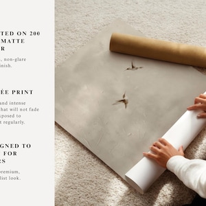 Op de afbeelding: Een persoon rolt een witte matte papieren print met twee kolibrie-illustraties. De print ligt op een lichtgrijze ondergrond, met een bruine papieren rol op de achtergrond. De tekst luidt "GEDRUKT OP 200 GSM MAT PAPIER".
