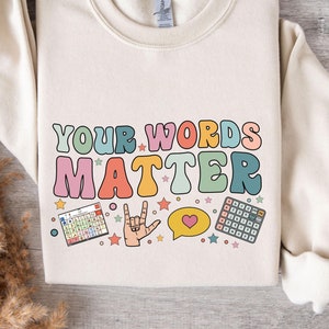 May include: A cream colored sweatshirt with the text "YOUR WORDS MATTER" in colorful letters. The text is surrounded by stars, a heart, a hand making the sign for "I love you", and two small squares with colorful squares inside.