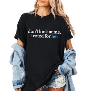 Peut inclure: T-shirt noir avec le texte "ne me regarde pas, j'ai vot&eacute; pour elle" en blanc et bleu.