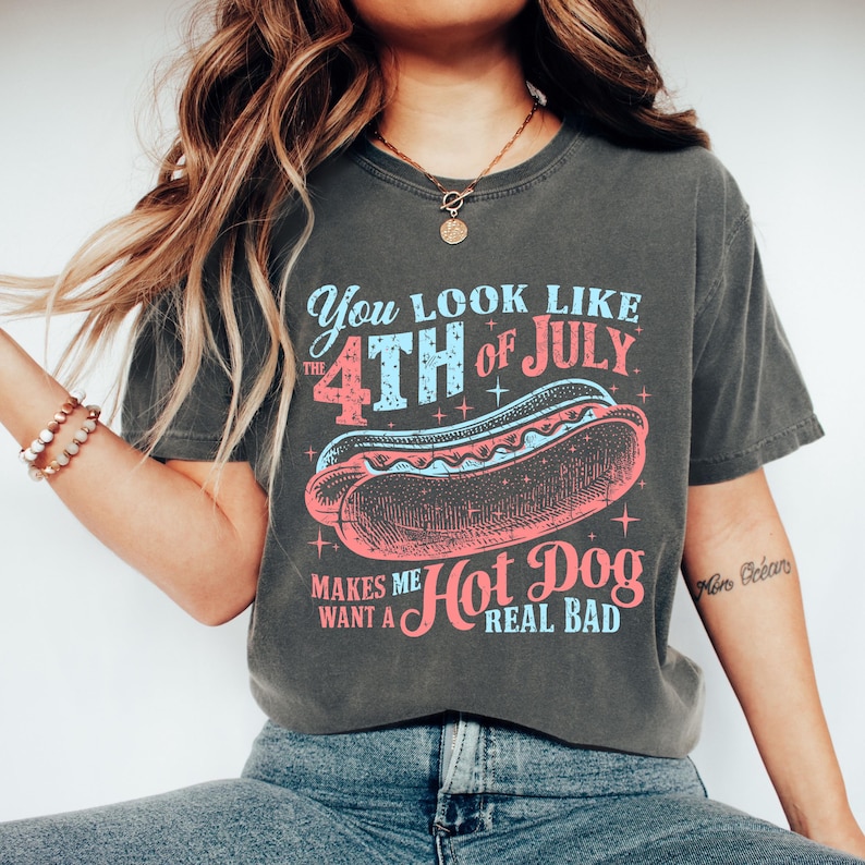 May include: A dark gray t-shirt with a vintage-style graphic that says "You look like the 4th of July makes me want a hot dog real bad". The graphic features a red, white, and blue hot dog with stars.
