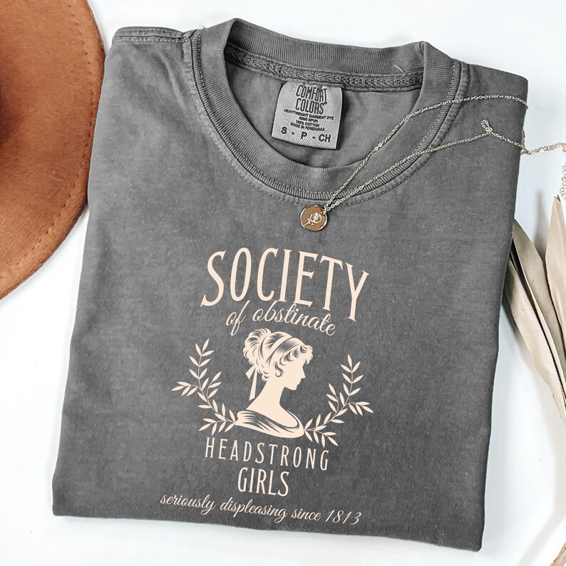 May include: Gray t-shirt with a vintage-style graphic that says "Society of Obstinate Headstrong Girls seriously displeasing since 1813".