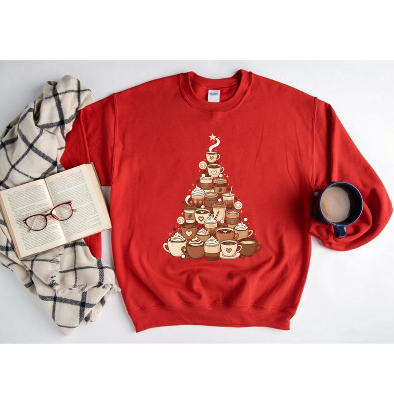 May include: A red sweatshirt features a Christmas tree design made of various coffee cups and mugs. The design includes different types of coffee drinks, such as lattes and cappuccinos. A star tops the tree. A book, glasses, and a mug are also in the image.