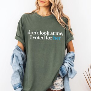 Peut inclure: Un t-shirt vert avec le texte "ne me regarde pas, j'ai vot&eacute; pour elle" en lettres blanches et bleues.