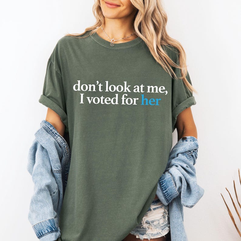Peut inclure: Un t-shirt vert avec le texte "ne me regarde pas, j'ai vot&eacute; pour elle" en lettres blanches et bleues.