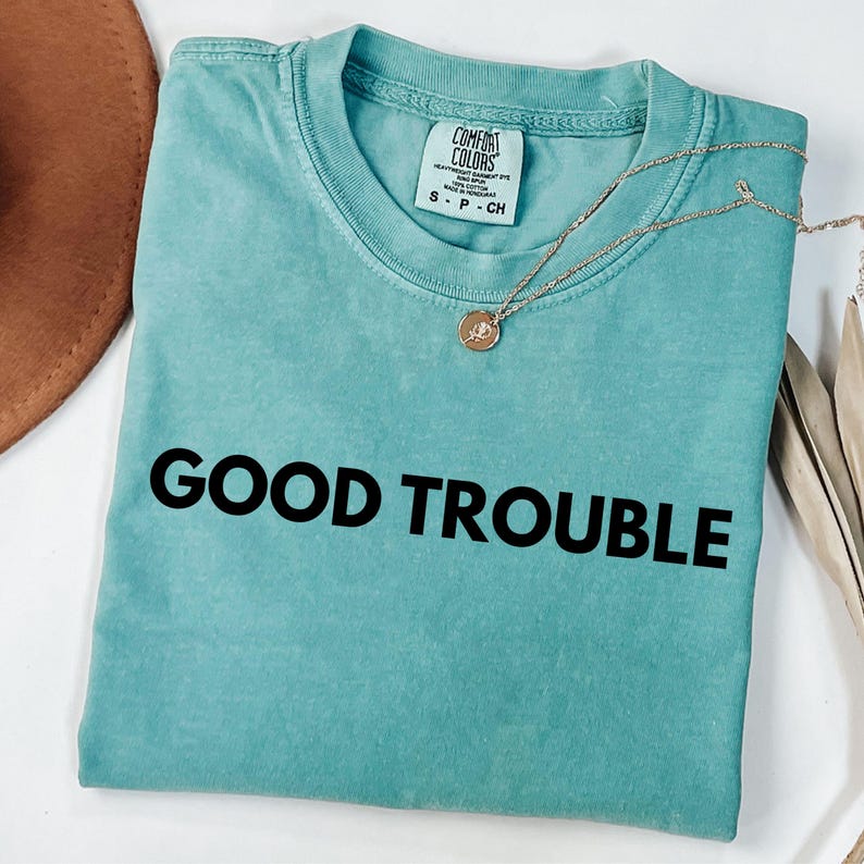 May include: A teal blue t-shirt with the text "GOOD TROUBLE" printed in black on the front.