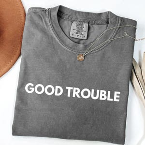 May include: Gray t-shirt with the text "GOOD TROUBLE" printed in white on the front.