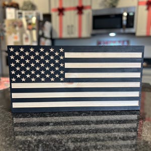 May include: A wooden American flag with black and white stripes and a field of stars. The flag is made of wood and has a distressed look.