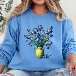 Puede incluir: Una sudadera azul claro con un gráfico de un ramo de iris azules en un jarrón amarillo.