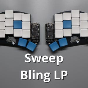 May include: A split keyboard with white and blue keycaps. The keyboard is black with a small circuit board on each side. The text "Sweep Bling LP" is displayed in white.