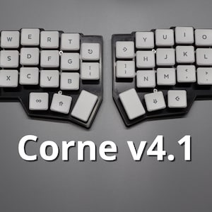 May include: A split mechanical keyboard with white keycaps and black frame. The keyboard is labeled "Corne v4.1". The keys are arranged in a split ergonomic layout, with each half angled. The keycaps have standard letter and symbol markings.