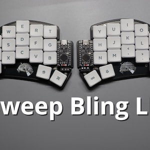 May include: A split keyboard with white keys and black lettering. The keyboard is labeled "Sweep Bling LP".