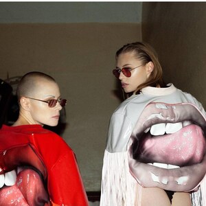 Puede incluir: Dos personas con chaquetas con grandes labios coloridos impresos en la espalda. La persona de la izquierda lleva una chaqueta roja con una lengua rosa, y la persona de la derecha lleva una chaqueta blanca con una lengua rosa.