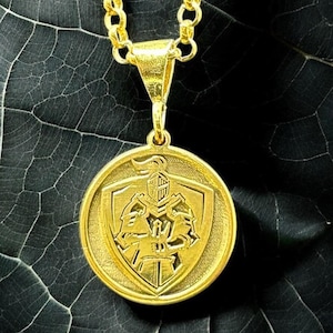 May include: A gold chain necklace with a round pendant featuring a knight in armor holding a sword. The pendant is on a dark background.