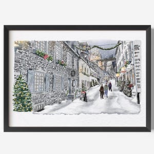 May include: Watercolor painting of a snow-covered street scene with stone buildings and Christmas decorations. A Christmas tree stands on the left. Several people are walking down the street. The artwork is framed in a black frame.