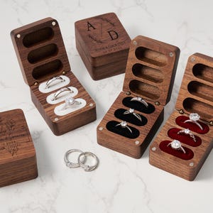 Könnte beinhalten: Drei Holzkästchen für Ringe mit Samt-Innenausstattung. Jedes Kästchen hat ein anderes Design und eine andere Inschrift. Ein Kästchen hat ein Blumenmuster und die Inschrift "Joanna & Gregory 19.10.2024". Ein anderes Kästchen hat ein Blumenmuster und die Inschrift "A & D Joanna & Gregory 19.10.2024". Das dritte Kästchen hat ein schlichtes Design mit der Inschrift "A & D".