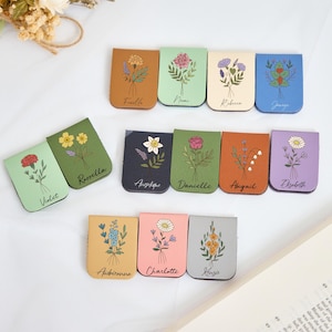 Può includere: Una collezione di segnalibri magnetici in pelle, ognuno con un'illustrazione floreale unica e un nome. I segnalibri sono in vari colori, tra cui verde, marrone e rosa. I disegni floreali includono rose, margherite e altri fiori selvatici.