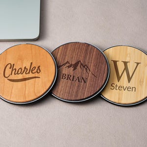 Pode incluir: Três bases de madeira redondas com borda preta. Uma tem o nome "Charles" gravado, outra um gráfico de montanha e o nome "Brian", e a terceira a letra "W" e o nome "Steven".