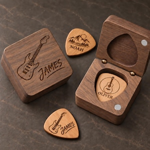 May include: A dark wood guitar pick box with a magnetic lid engraved with an electric guitar and the name James. Two additional wooden guitar picks are included, one engraved with a mountain scene and the name Noah, and one with an acoustic guitar and the name Oliver, which rests inside an open matching wooden box.