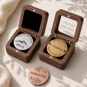 May include: Two square dark wood boxes with hinged lids, one containing a silver coin engraved with a mountain and the name BRIAN, the other a gold coin engraved with ANDREW and the text Who will decide? Flip to decide. A copper coin with floral designs and the name SAMANTHA sits in front.