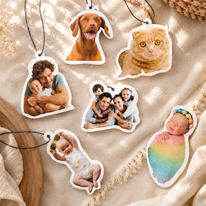 May include: A collection of six custom photo ornaments featuring various subjects including a brown dog, a ginger cat, a man holding a baby, a family of four, a baby wearing yellow sunglasses, and a newborn wrapped in a rainbow blanket.