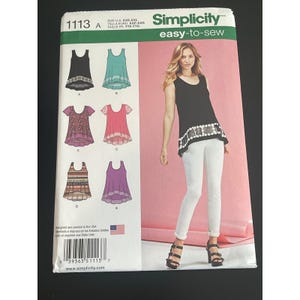 May include: Simplicity easy-to-sew pattern 1113 features various top designs. The pattern includes illustrations of tops in black, teal, pink, purple, and patterned fabrics. The cover also shows a woman wearing a black top and white pants.